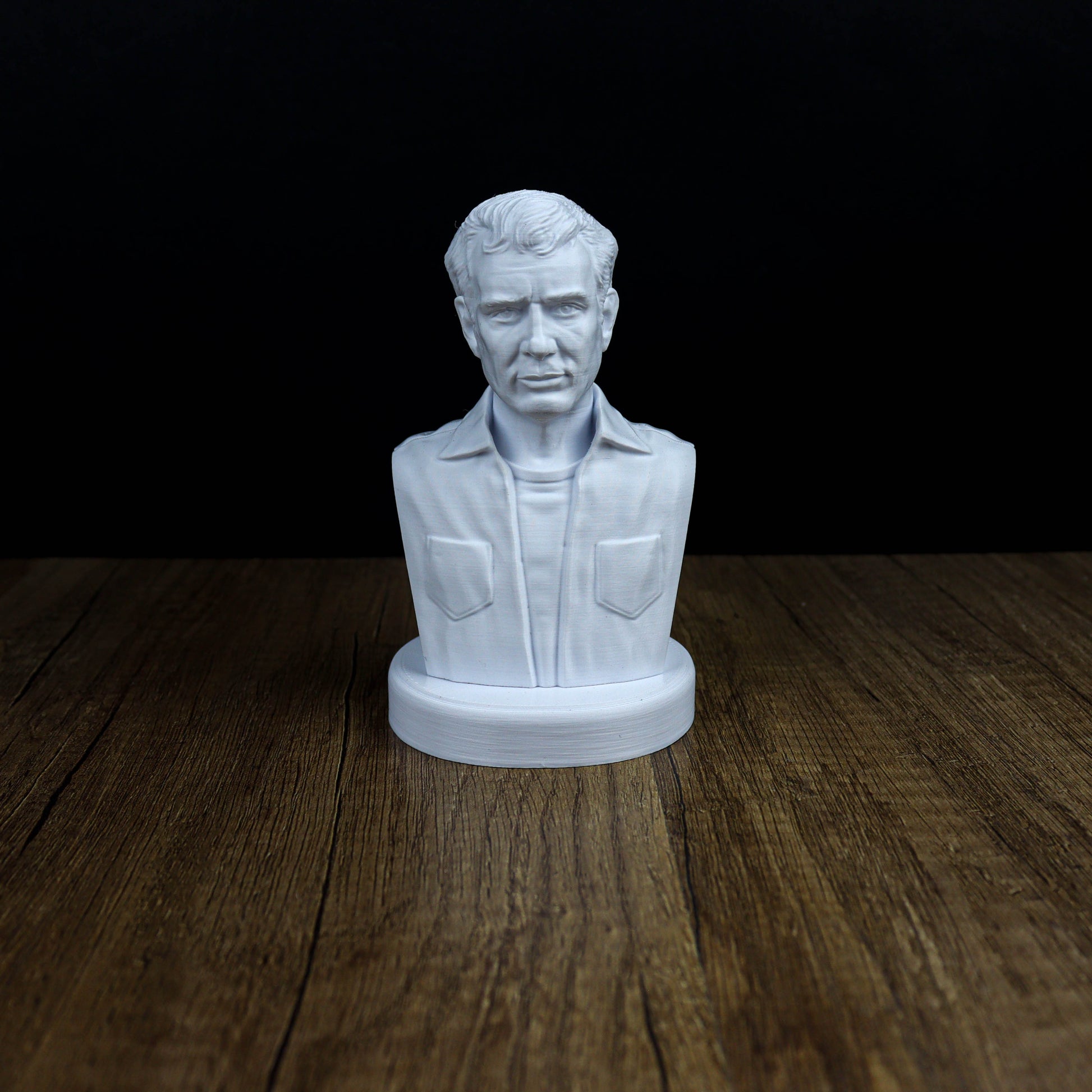 A white bust of a man is displayed on a wooden surface against a black background.